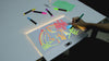 A hand drawing an illuminated design on the reusable Meshkat Glow Board